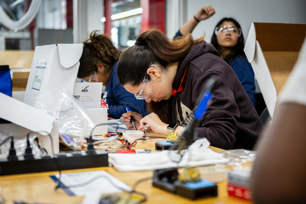 female students with eye protective gear conducting assignments with electronic tools.