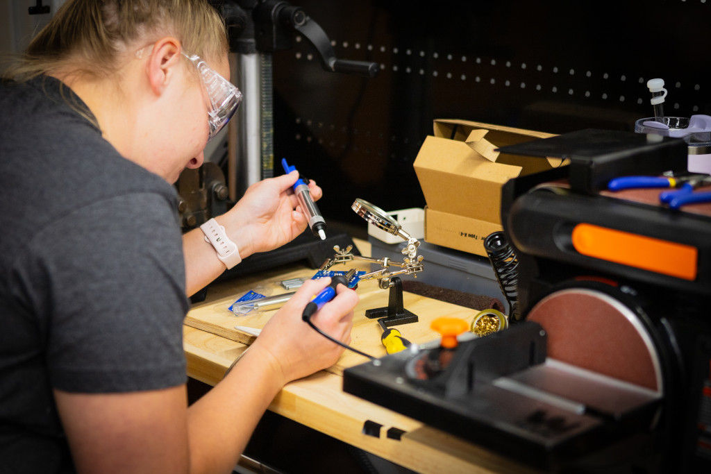 female student with protective eye gear conducting research with electronic tools at a station.