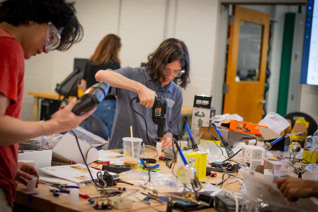 two male students with drills conducting research and assignments with safety glasses on.